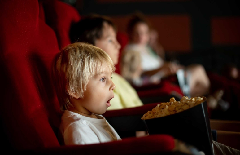 Cute child, boy, watching movie in a cinema, eating popcorn and enjoying