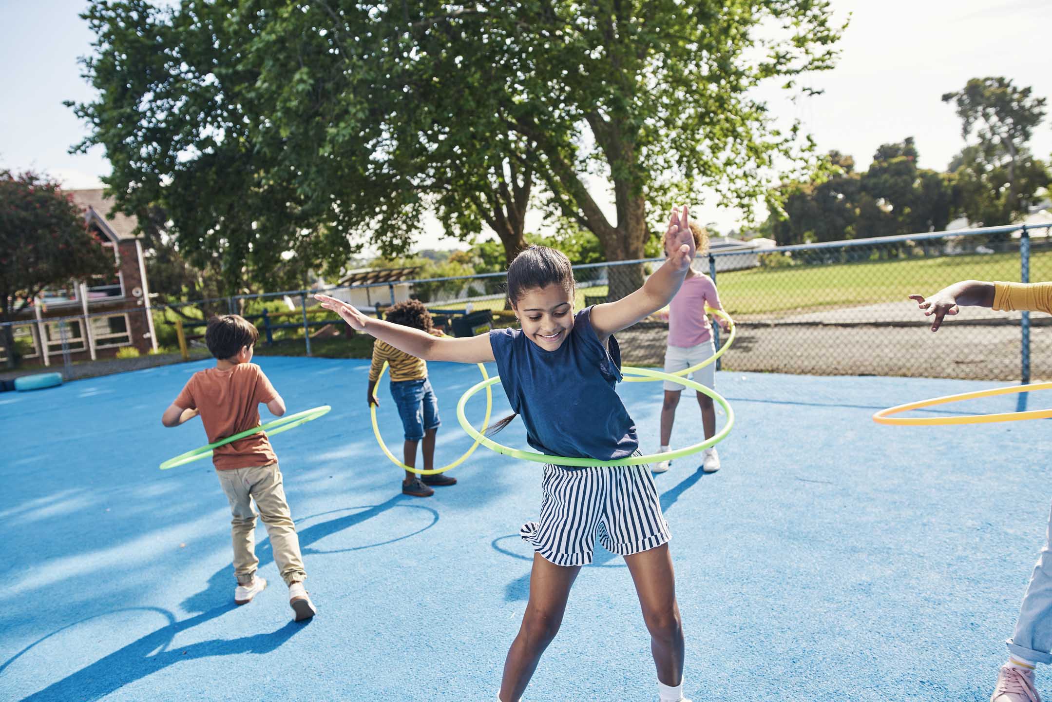 Children, hula hoop and friends playing outdoor together during break or recess on a school playground