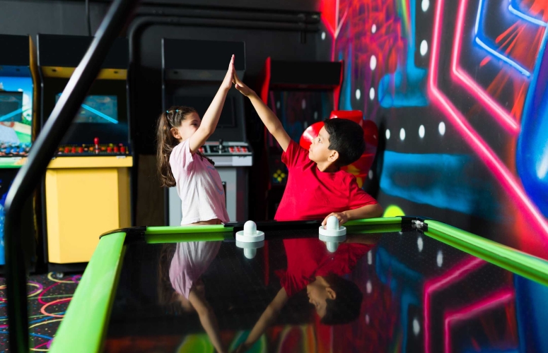 Cheerful children playing air hockey at the arcade