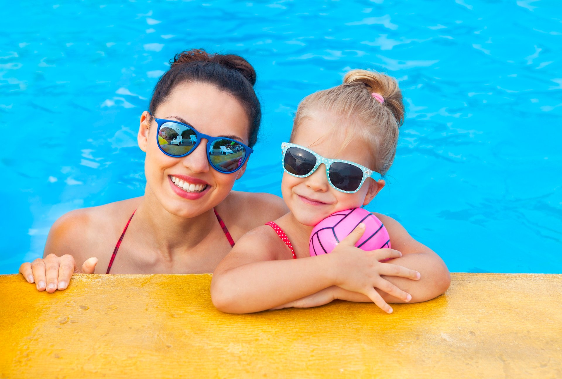 Happy mother and little daughter having fun in swimming pool