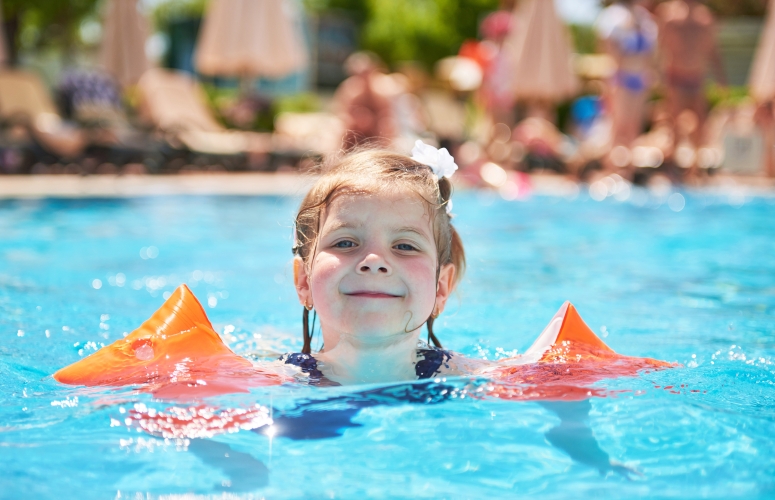 Girl swimming in the pool in armlets on a hot summer day.
