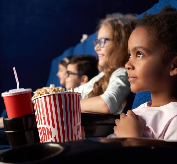 Kids gleefully watching a movie together, with popcorn and fountain drinks.