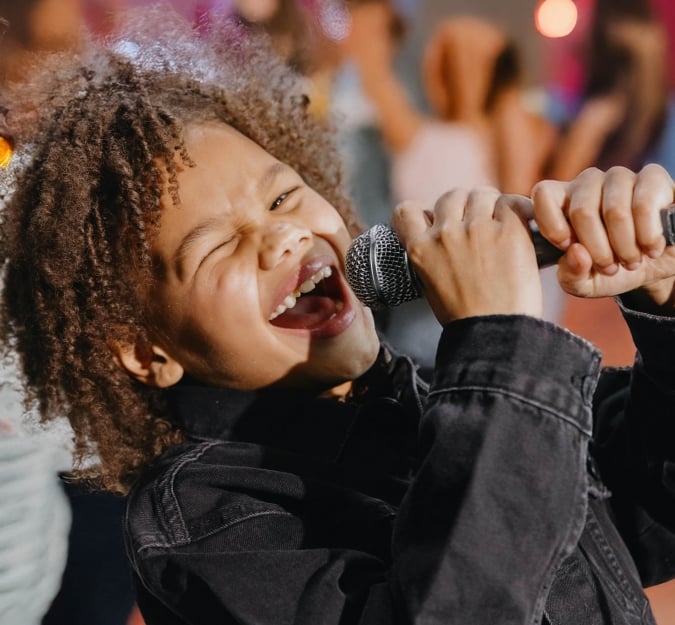 Child dressed in black denim sings passionately into the microphone