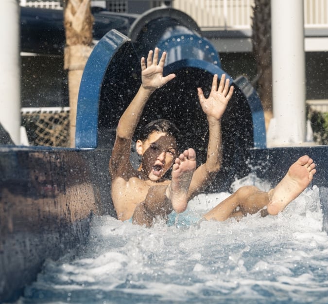A boy laughs as he rides down a water slide