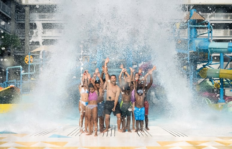 A large group of individuals stand under The Tipping Bucket as water pours over them, at Surf and splash Waterpark