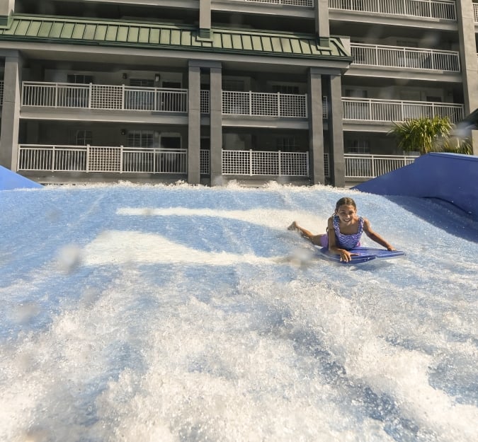 A girl on a surf board rides the Flow Rider attraction at Surf and Splash Orlando