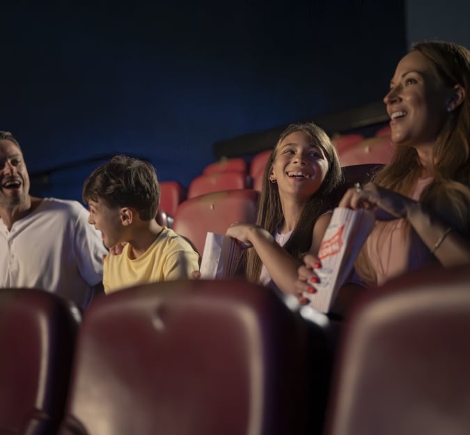 A family of four laughing, eating popcorn, at the Movie Theater